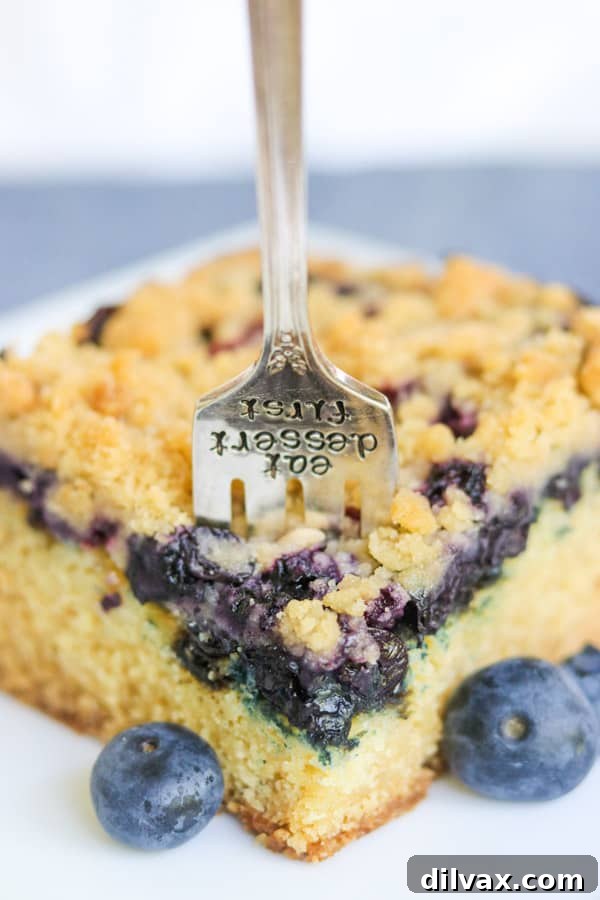 A fork taking a bite from a moist slice of blueberry crumb cake.