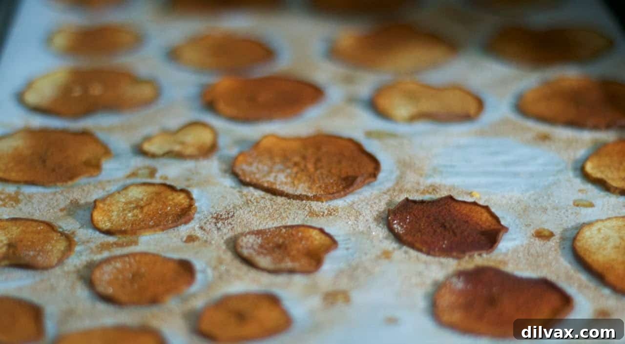 A close-up of baked cinnamon pear slices on a baking sheet, golden and slightly curled.