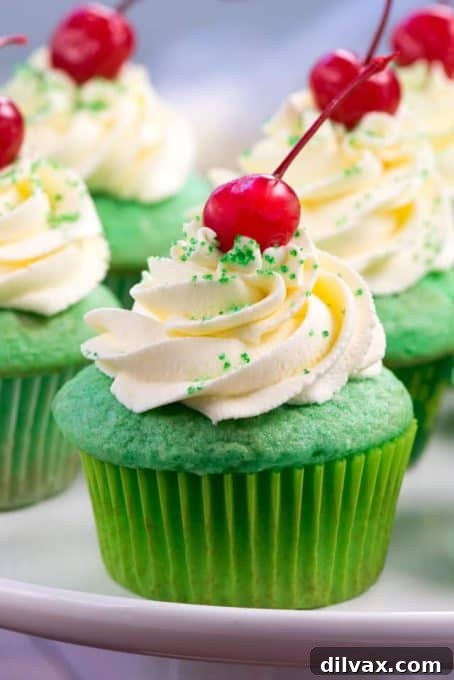 Fluffy green cupcakes topped with white whipped frosting and a cherry, mimicking a classic Shamrock Shake.