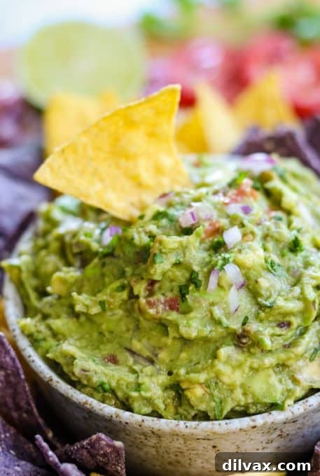 A crunchy tortilla chip perfectly dipped into a vibrant bowl of chunky, fresh homemade guacamole, ready for snacking.