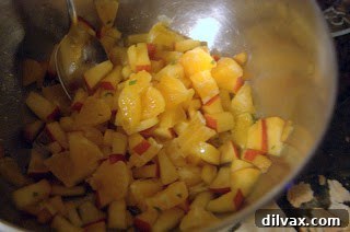 Diced peaches and oranges mixed with mint and sugar in a bowl