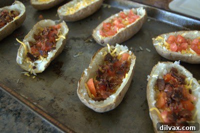 Potato skins loaded with cheese, bacon, and tomatoes on a baking sheet.