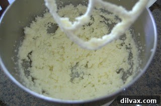 Butter and sugar being creamed together in a white mixing bowl, showing a pale, fluffy texture