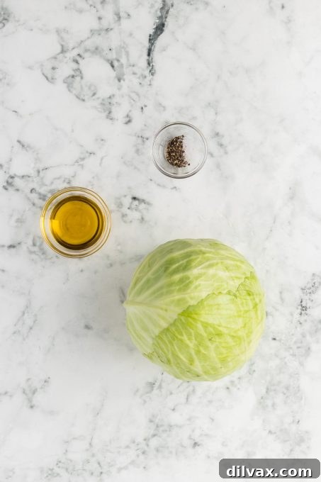 Crispy Roasted Cabbage Steaks 4 A fresh head of green cabbage, a bottle of olive oil, a shaker of salt, and a pepper grinder on a wooden surface.