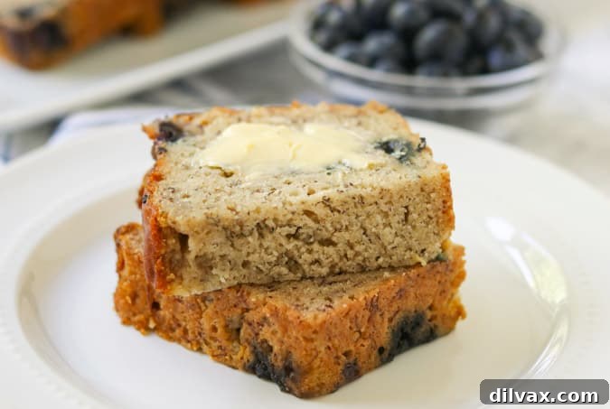 A buttered slice of moist blueberry banana bread on a wooden board, with fresh blueberries scattered in the background, inviting a delicious bite.