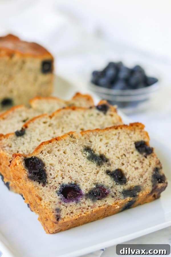 Beautifully sliced quick bread, showing off the perfectly distributed blueberries baked into the moist banana bread, presented on a plate with fresh blueberries.