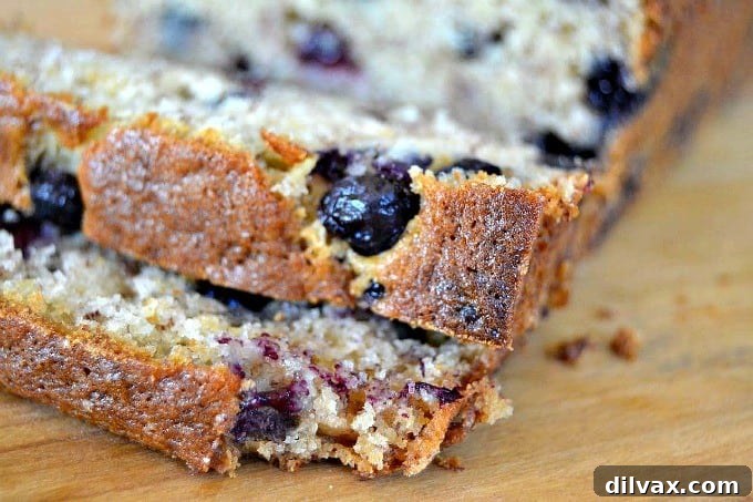 Close-up shot of a single vibrant blueberry perfectly baked into a slice of moist banana bread, highlighting the texture and juicy fruit.