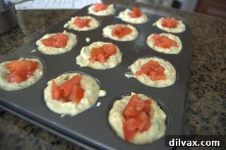 Zucchini Bites batter in muffin tin with diced tomatoes placed on top before baking