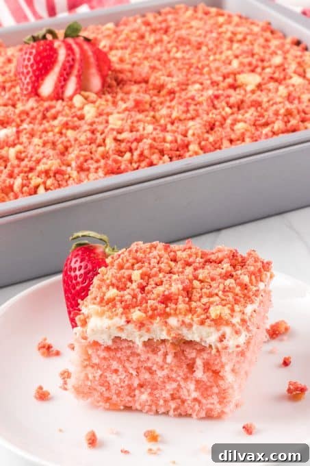 Divine Strawberry Crunch Cake 13 A pink strawberry flavored cake on a plate with a strawberry in front of a cake pan.