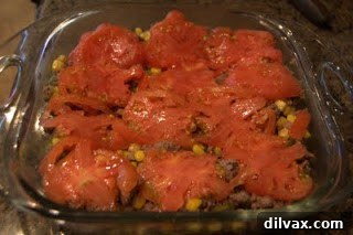 Beef and corn mixture covered with sliced tomatoes in a baking dish.
