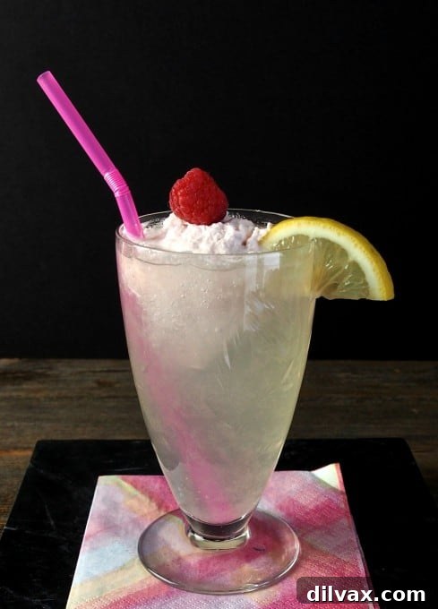 Homemade Lemonade with Raspberry Cream, a creamy pink drink garnished with raspberries and lemon.