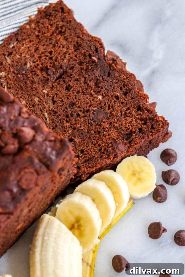 Decadent Double Chocolate Banana Loaf 5 A perfectly sliced piece of Double Chocolate Banana Bread, moist and rich with chocolate, presented alongside fresh sliced banana and a scattering of semi-sweet chocolate chips.