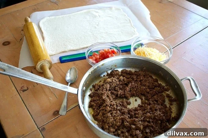 Parchment paper with pizza dough, showing cuts made along the sides for braiding, filled with taco meat, cheese, and tomatoes.