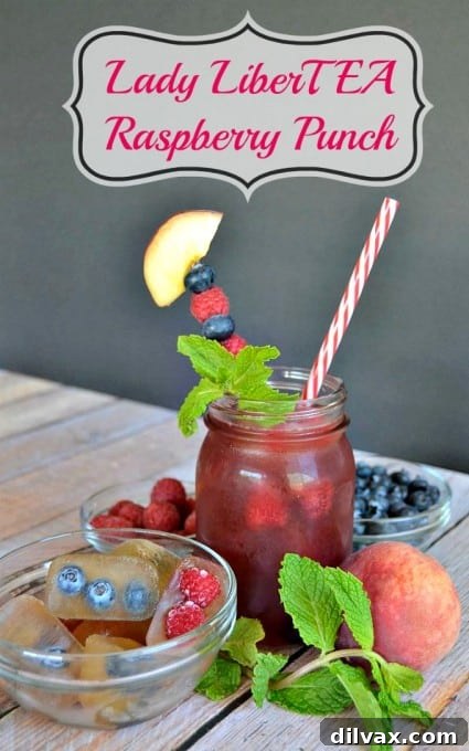 Close-up of a refreshing glass of Lady LiberTEA Raspberry Punch with berry ice cubes and fresh fruit garnish.