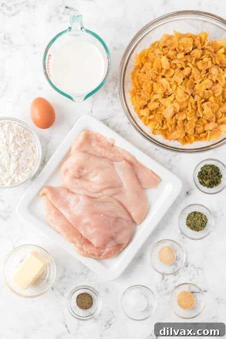 Assorted ingredients for Cornflake Chicken including fresh chicken, cornflakes, butter, milk, flour, herbs, and spices laid out on a table