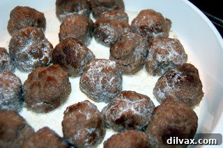 Browned meatballs in a casserole dish with beef broth.