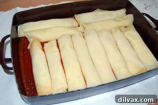 Rolled manicotti arranged in a baking dish over a layer of sauce.