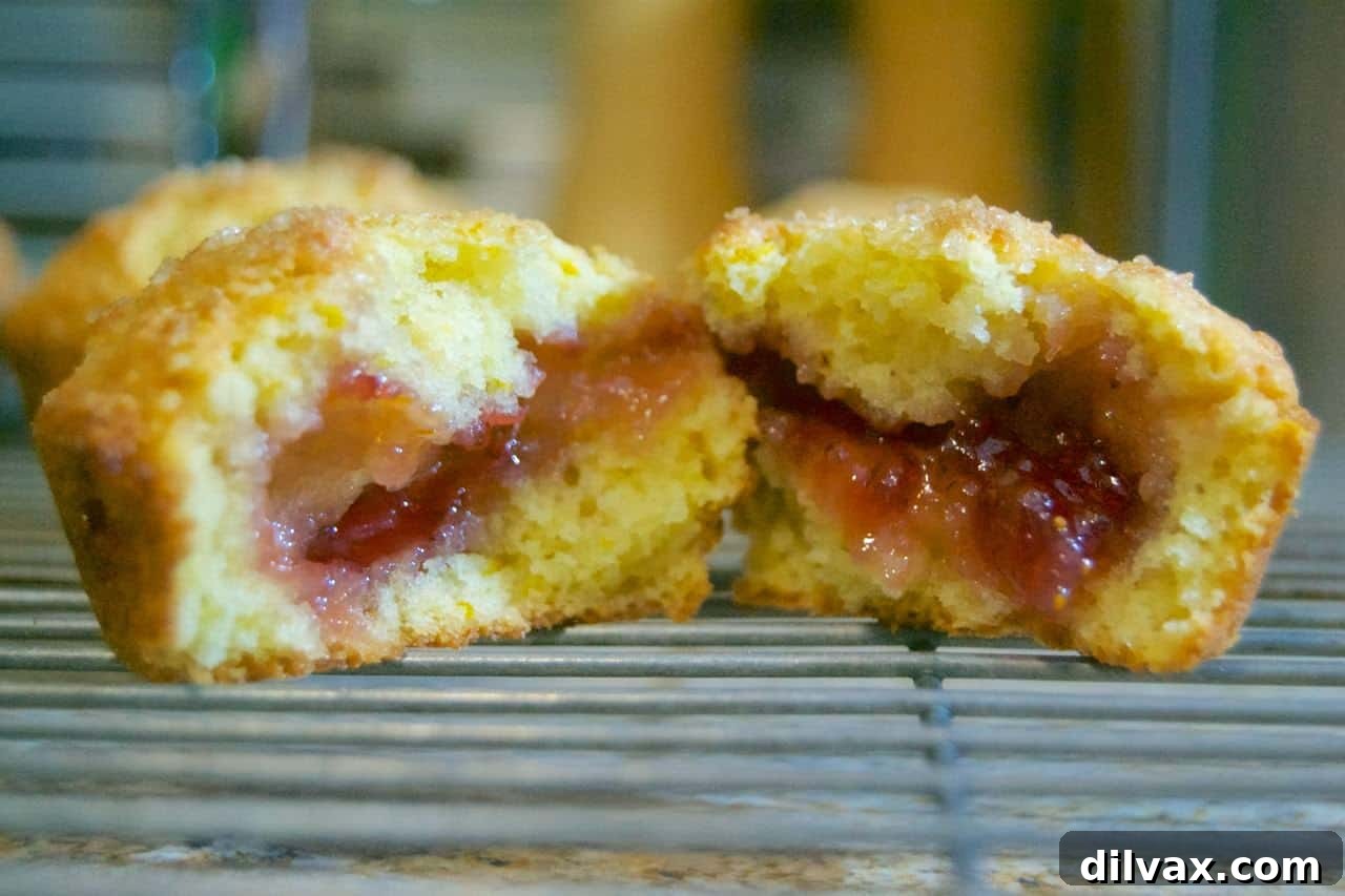 Beautifully baked Orange Ricotta Muffins with Strawberry Jam on a cooling rack.