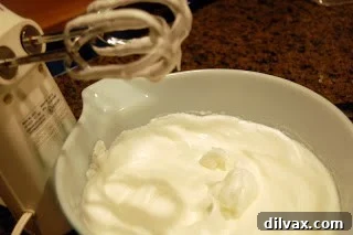 Beating egg whites with sugar until stiff peaks form, crucial for soufflé structure.