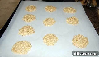 Sweet Pignoli Perfection 5 Dough balls coated with pine nuts, placed on parchment paper lined baking sheet.