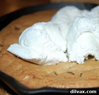 Warm chocolate chip pizookie in a cast iron skillet topped with melting vanilla ice cream.