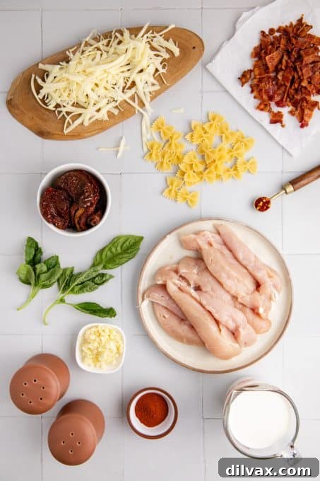 Array of fresh ingredients laid out on a wooden board, including minced garlic, a jar of sun-dried tomatoes, raw chicken tenders, spices, half-and-half, shredded mozzarella, and dried basil for Chicken Mozzarella Pasta.