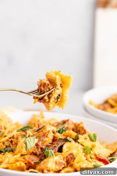 Close-up of a fork taking a bite of creamy Chicken Mozzarella Pasta, showing the intertwined pasta, chicken, and sun-dried tomatoes.