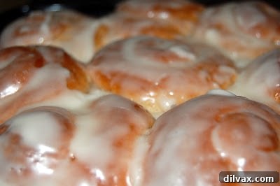 Freshly baked cinnamon rolls with a thin layer of glistening glaze applied, hot from the oven.