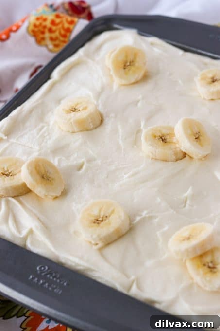 Golden Banana Cake with Velvety Cream Cheese Frosting 6 A slice of banana cake topped with cream cheese frosting and a sprinkle of cinnamon, served on a white plate.