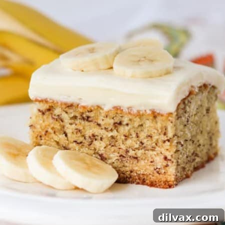 Golden Banana Cake with Velvety Cream Cheese Frosting 8 A mouthwatering slice of banana cake with cream cheese frosting on a plate, with whole bananas in the background.