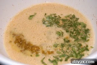 Day 21: Chile Cheese Casserole Magic 3 Diced green chiles and fresh cilantro being added to a bowl containing a mixture of eggs, egg whites, chili powder, and pepper.