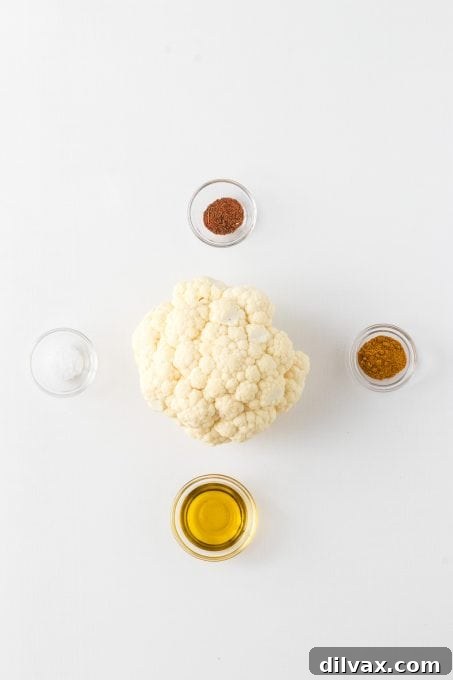 Cajun Curry Roasted Cauliflower 4 Ingredients laid out for Roasted Curry Cajun Cauliflower recipe: a head of cauliflower, olive oil, curry powder, and Cajun seasoning.