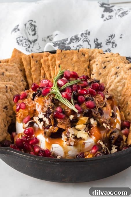 Melted Brie Bliss 7 A whole baked brie wheel with golden-brown crust and melted interior, topped with a colorful array of dried fruits and nuts.