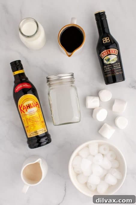 Ingredients for a Frozen Marshmallow Mudslide laid out on a table: bottles of liquor, milk, ice, chocolate syrup, and marshmallows.