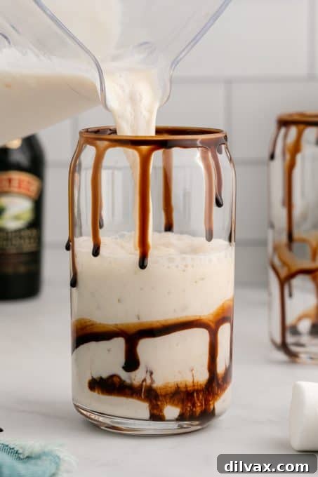 A Frozen Marshmallow Mudslide being poured from a blender into a chocolate-rimmed glass.