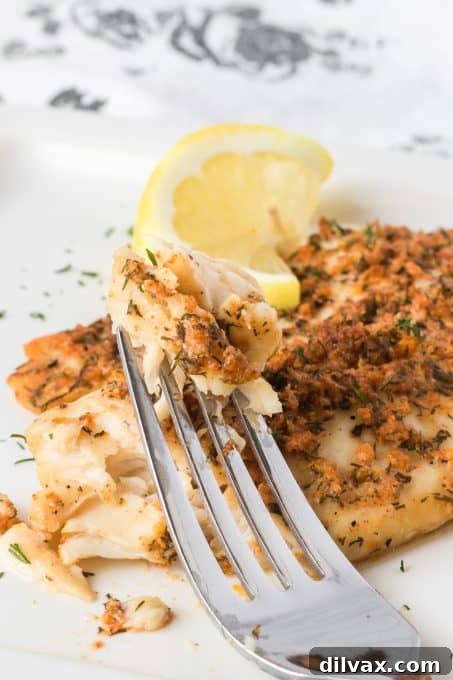A fork taking a bite of steamed, seasoned tilapia from a plate.