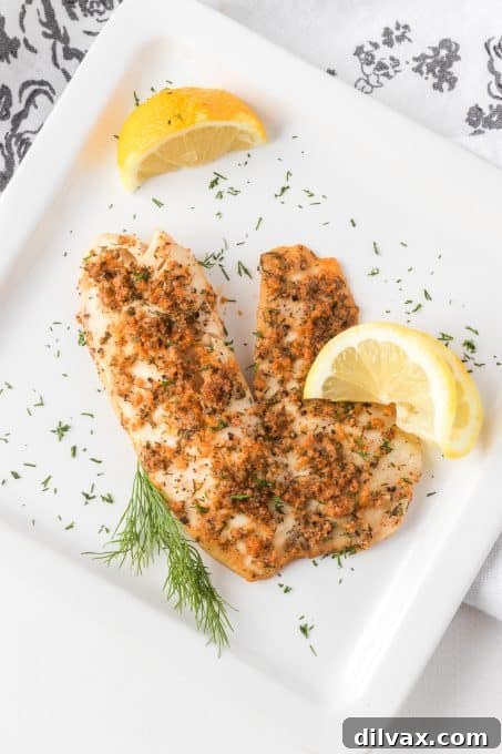 Plated steamed tilapia fillet with fresh herbs and lemon slices, ready to be eaten.