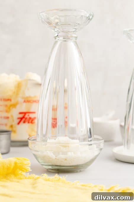 Applying shredded coconut flakes to the rim of a milkshake glass using cream of coconut.