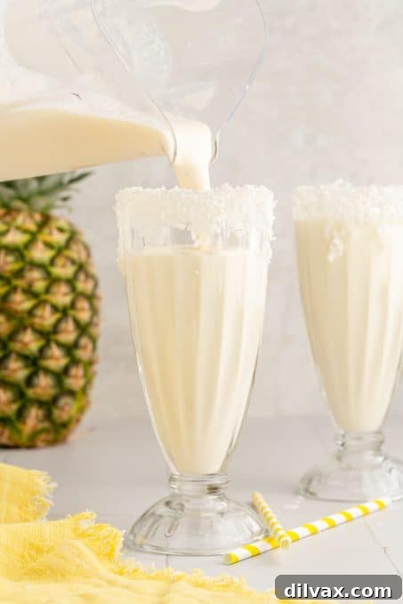 Pouring a freshly blended Pina Colada Milkshake into a tall, garnished glass.