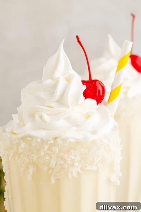 A Pina Colada Milkshake topped with whipped cream and a cherry, with coconut flakes on the rim.