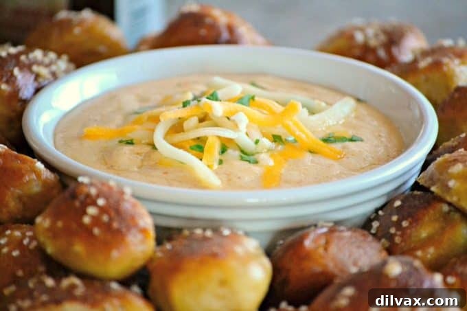 A close-up shot of the Beer Cheese Dip with a single homemade pretzel bite dipped in it, showcasing its creamy texture.