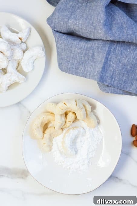 Almond crescent cookies being coated in powdered sugar.