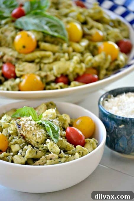 Overhead view of a beautifully presented Pesto Chicken Pasta Salad, featuring campanelle pasta, tender chicken pieces, halved cherry tomatoes, and creamy mozzarella, all coated in a rich green pesto sauce. Garnished with fresh basil leaves.