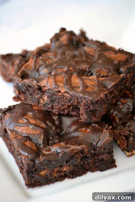 Close-up of a square of Chocolate Overload Loaded Brownies, showing the rich chocolate base, visible candy pieces, and a generous drizzle of chocolate sauce and frosting, ready to be enjoyed.
