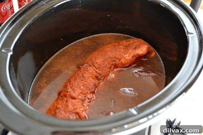 Sweet Heat Cola Pulled Pork Bites 7 The pork loin nestled in a slow cooker, covered with barbecue sauce and Coca-Cola, slow-cooking to perfection.