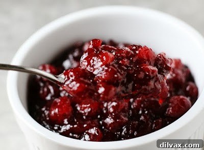Vibrant simple whole berry cranberry sauce in a white bowl, garnished with fresh cranberries.
