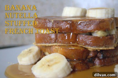 Two pieces of golden brown Banana Nutella Stuffed French Toast, drizzled with maple syrup and powdered sugar, on a white plate with fresh berries.