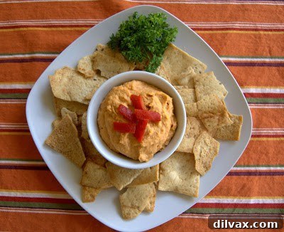 Velvety Roasted Garlic Hummus 7 A vibrant bowl of Roasted Red Pepper and Garlic Hummus, swirled with olive oil and garnished with fresh herbs, served alongside crispy bread and colorful vegetables.