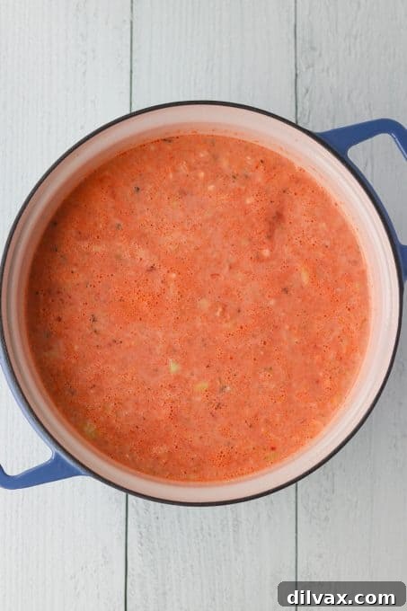 A ladle serving a generous portion of creamy tomato basil soup into a rustic ceramic bowl, highlighting the soup's smooth, rich consistency.