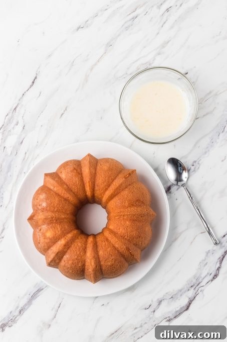 Gigi's Effortless Lemon Cake 8 A freshly baked golden-brown bundt cake cooling on a wire rack, with a small bowl of lemon glaze nearby, ready for its final touch.